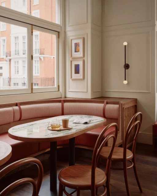 Corner booth seating in a restaurant with an oval marble-topped table set for dining, wooden chairs, and a warm, inviting atmosphere.
