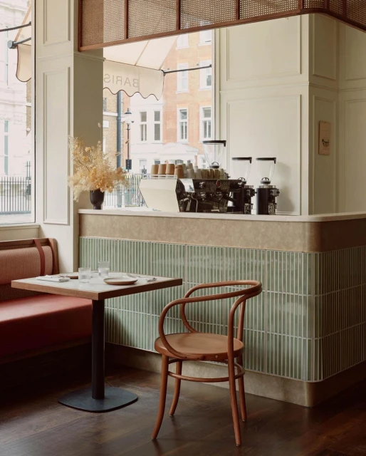 Interior view of a cafe featuring a table with glasses, a bentwood chair, a banquette seat, and a coffee machine on the counter.
