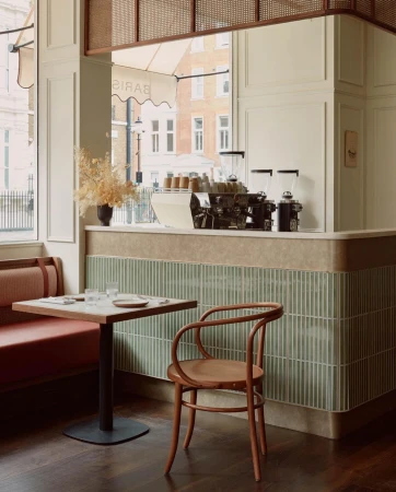 Interior view of a cafe featuring a table with glasses, a bentwood chair, a banquette seat, and a coffee machine on the counter.