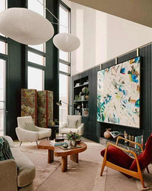 Living room interior with high ceilings, featuring a diverse collection of furniture, an abstract art piece, and modern pendant lighting.