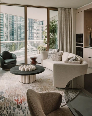 Modern apartment interior featuring a neutral curved sofa, round coffee table, cityscape view through large windows, and stylish decor.