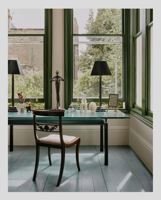 Interior view of a desk with lamps, a sculpture, and a chair by a window, showcasing a blend of classic and modern design elements.