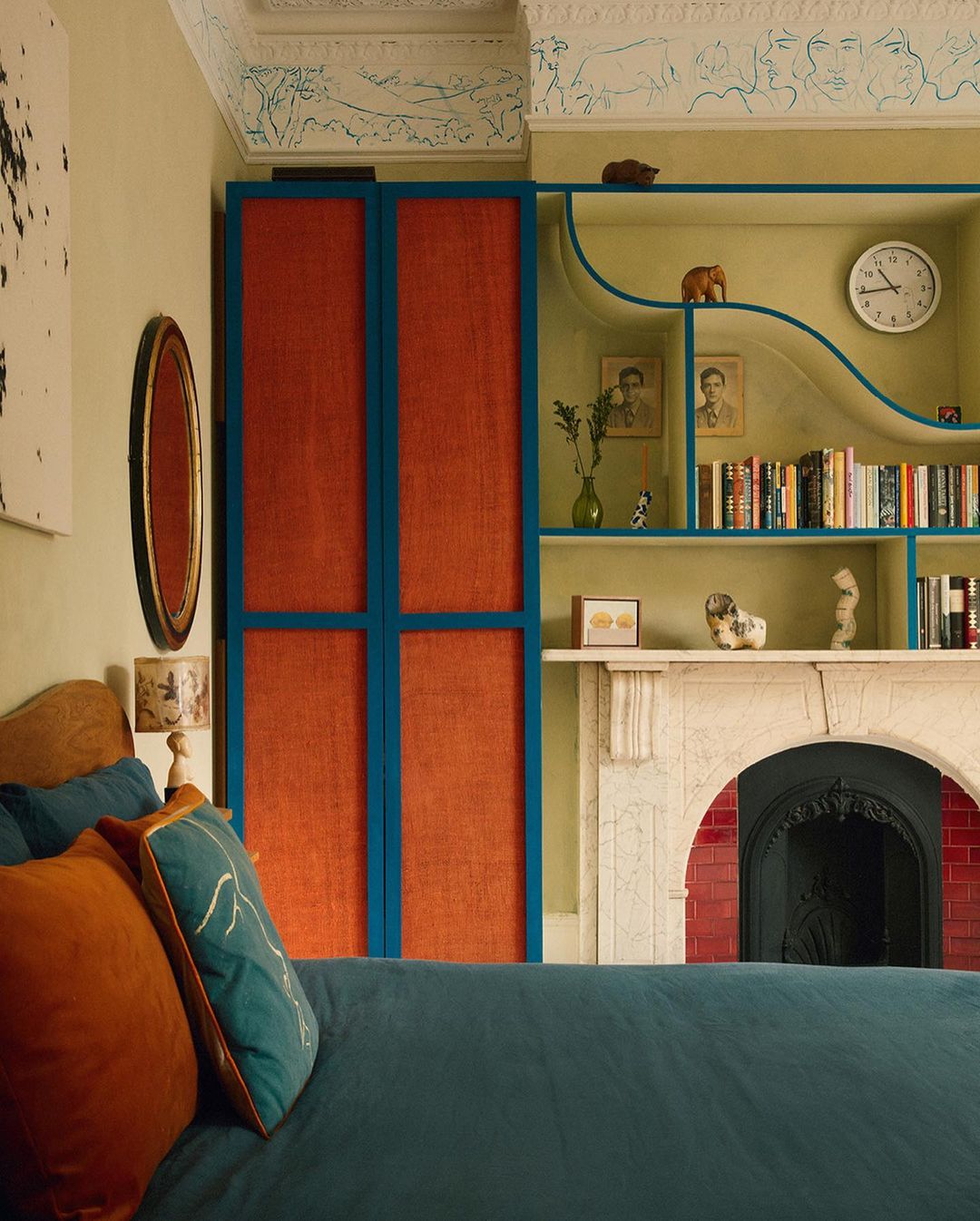 Eclectic bedroom interior featuring a blue bedspread, orange pillows, a colorful wardrobe, and stylish built-in bookshelves.