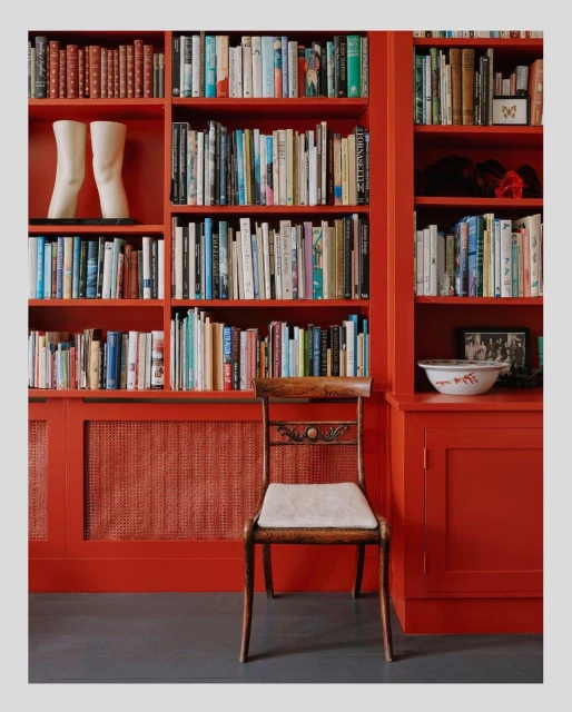 Brightly colored bookshelf with books, a chair, and a pair of white leg sculptures in an indoor environment with natural lighting.
