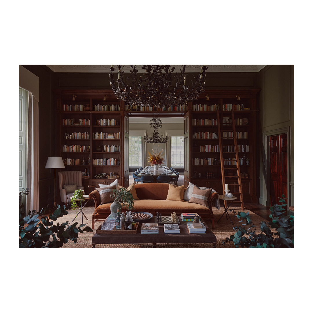 Living room interior with a brown sofa, bookshelf, and chandelier; a stylish and cozy space for relaxation and reading.