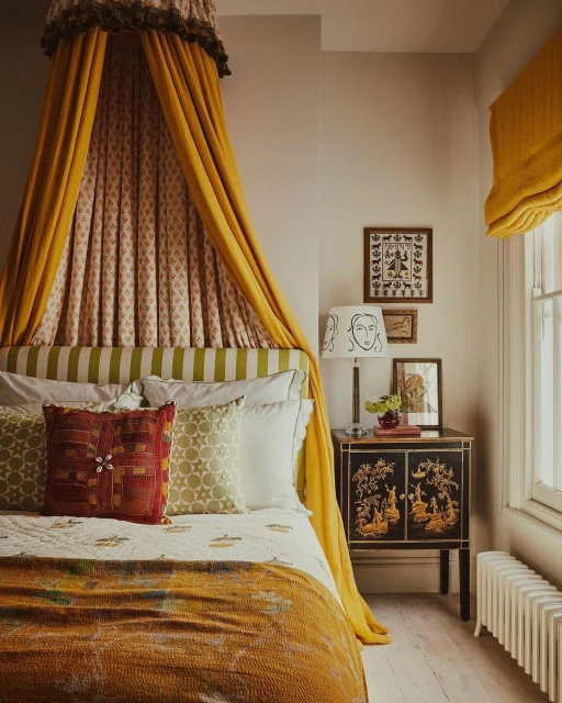 Cozy bedroom interior with a yellow canopy bed, patterned pillows, a dark wood cabinet, and decorative wall art.