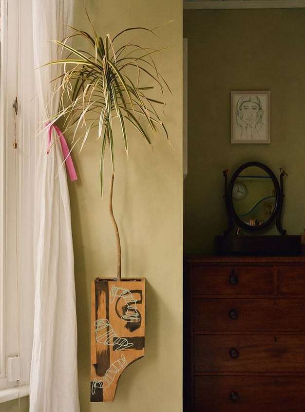 Indoor shot of potted houseplant displayed on a wall-mounted wooden shelf with painted designs, next to a vintage dresser.