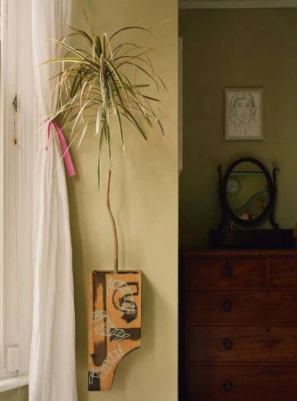 Indoor shot of potted houseplant displayed on a wall-mounted wooden shelf with painted designs, next to a vintage dresser.