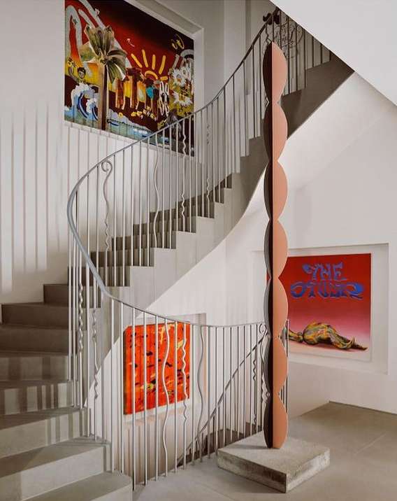Interior staircase with a modern sculpture on a stone base, complemented by colorful abstract art on the surrounding walls.