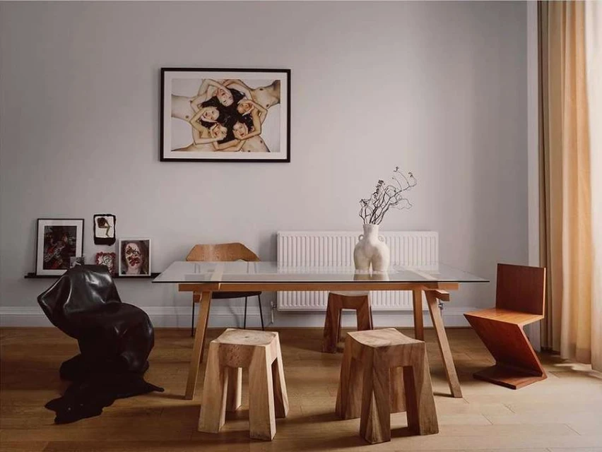 Interior of a dining room with a wooden table and chairs, artwork on the wall, and a unique black leather chair.