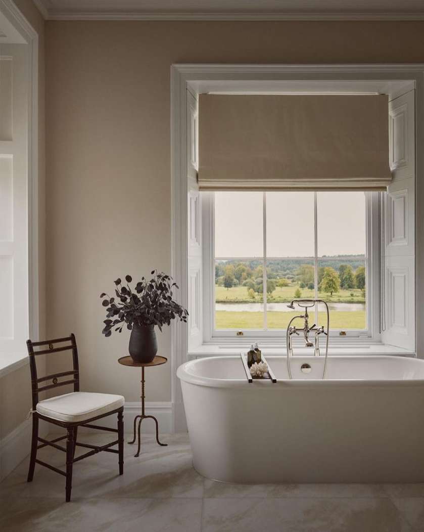 Classic white bathtub by a window with greenery. Bathroom interior featuring neutral colors and natural light.