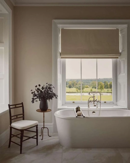 Classic white bathtub by a window with greenery. Bathroom interior featuring neutral colors and natural light.