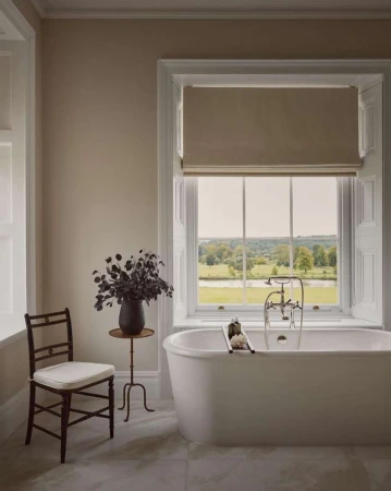 Classic white bathtub by a window with greenery. Bathroom interior featuring neutral colors and natural light.