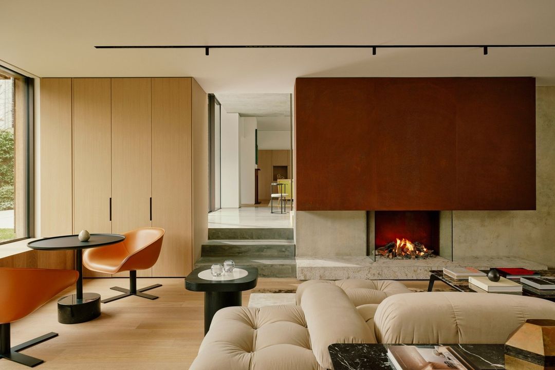 Interior view of a modern living room featuring a beige sectional sofa, fireplace with a brown metal surround, and contemporary furniture.