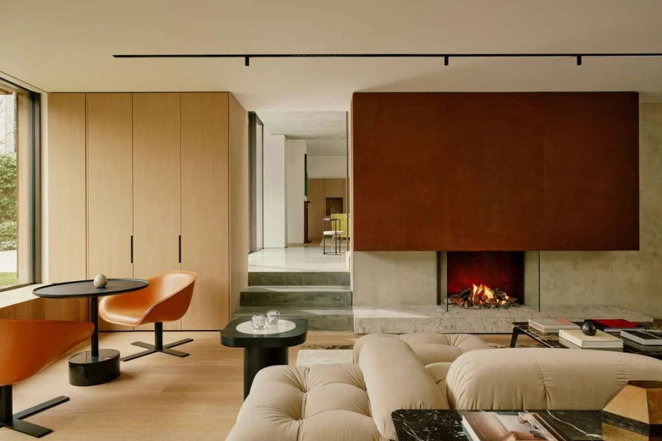 Interior view of a modern living room featuring a beige sectional sofa, fireplace with a brown metal surround, and contemporary furniture.
