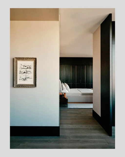 Hallway view into a modern bedroom with a framed artwork of reclining figures hanging on the wall, wood floors and trim details.