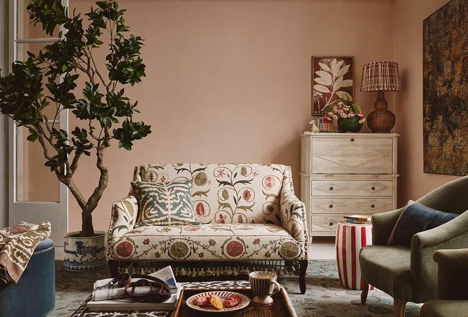 Living room interior with a floral loveseat, green armchairs, and potted tree, creating a warm, inviting, and elegant home space.