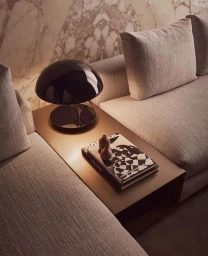 Modern interior corner with a light beige fabric sofa, metallic bronze side table, black glossy mushroom lamp, and art books on the table.