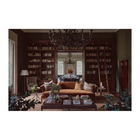 Spacious dark green library interior featuring a warm brown velvet sofa, low coffee table, and tall wooden bookshelves.