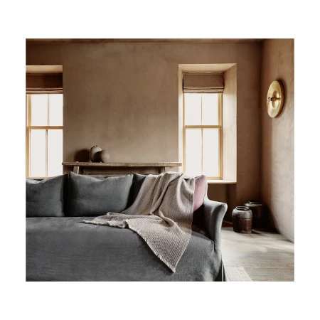 Dark grey sofa with a textured light throw blanket in a warm earth-toned interior with two windows and rustic pottery.