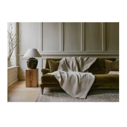 Olive green velvet sofa with a ribbed cream throw blanket and matching cushions in a paneled living room by Kensington Leverne