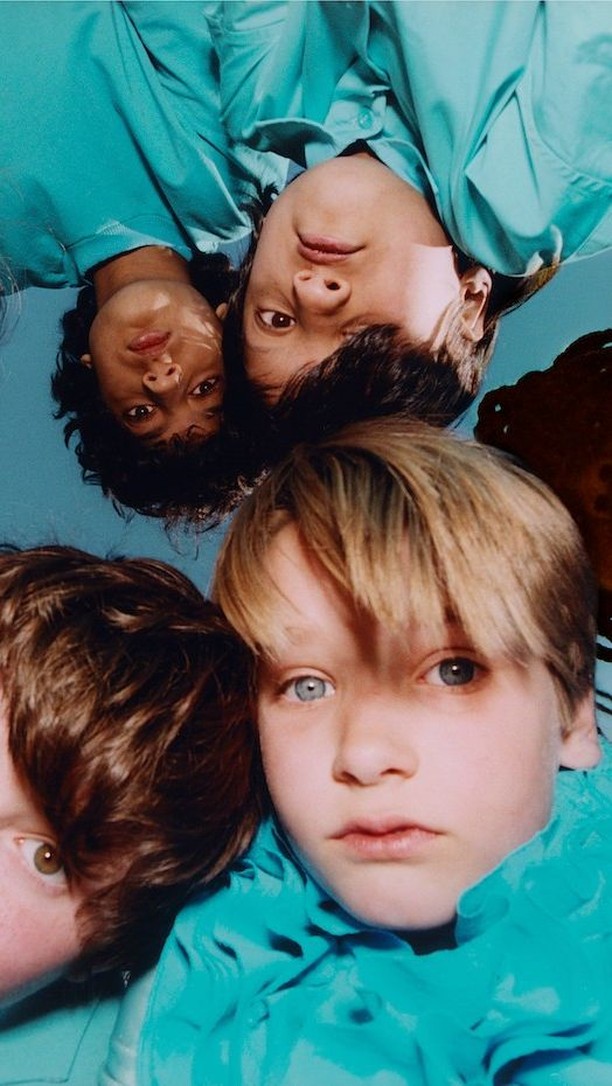 Close-up of three children, including a child with heterochromia, wearing matching turquoise shirts, shot from a high angle indoors.