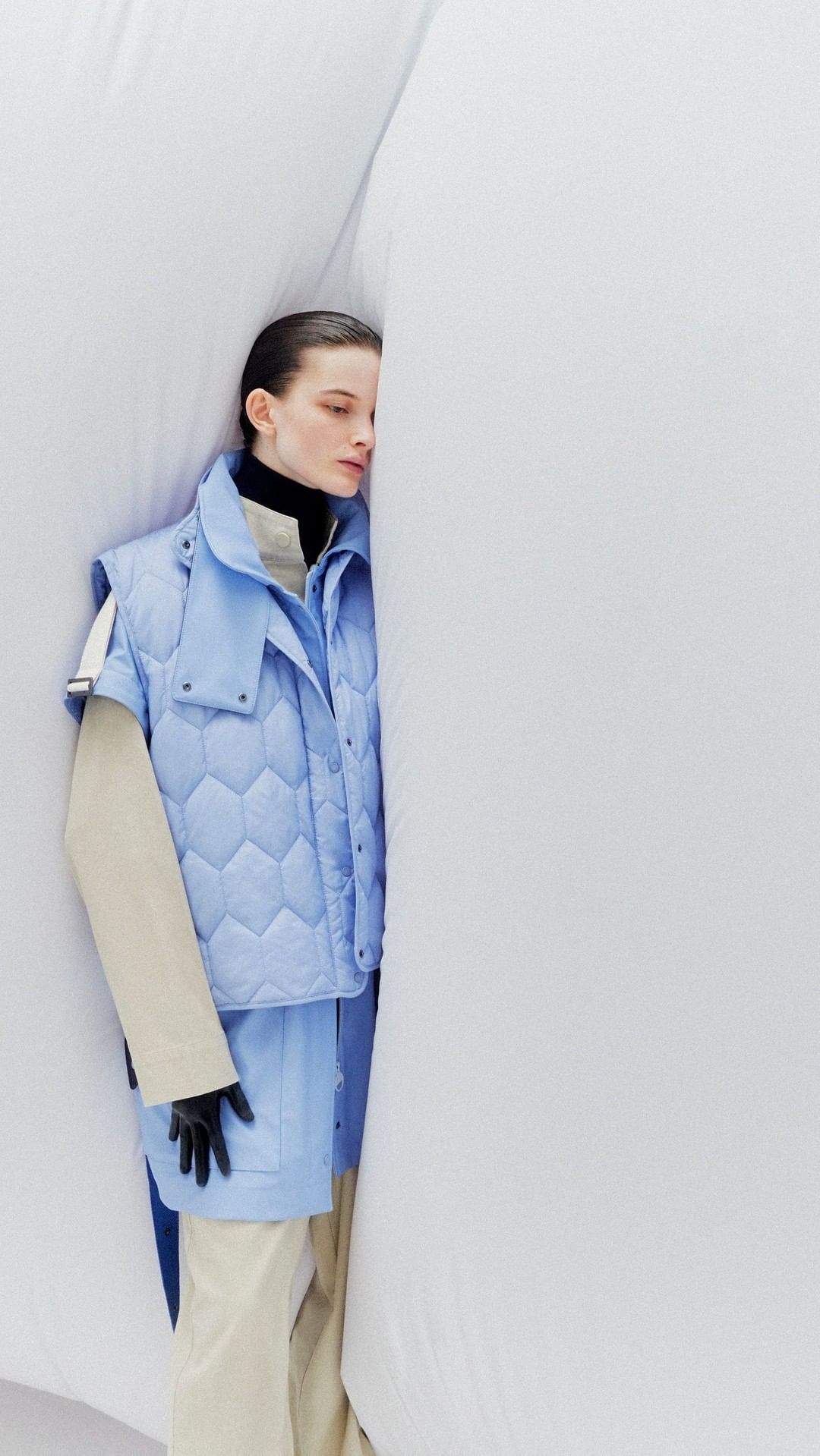 Fashion photography showcasing a young woman wearing a light blue quilted vest and matching skirt against a textured white background.