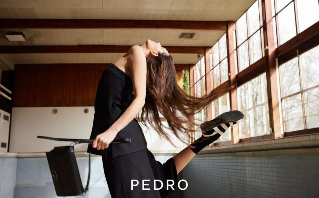 Fashion shot of a woman in a black outfit in an abandoned pool, modeling a black purse while one leg is raised in the air.