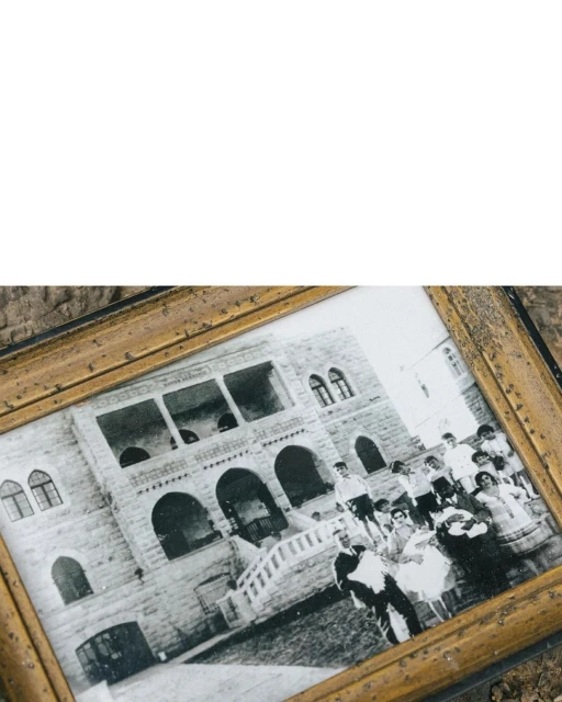 Framed black and white photo displays a large group of people standing in front of a stone building with arched windows and a staircase.