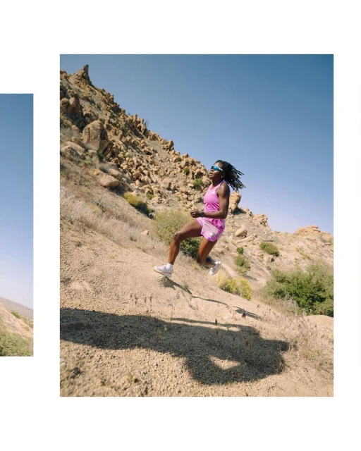 Athletic black woman running downhill on a rocky, arid landscape under a blue sky, wearing athletic gear and sunglasses.