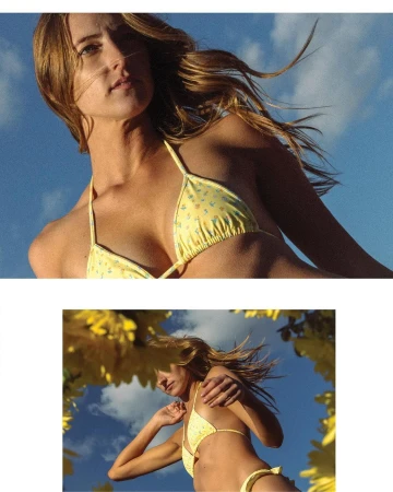 A woman in a yellow bikini stands beneath a clear sky, framed by yellow flowers. Shot from a low angle, summertime fashion shoot.