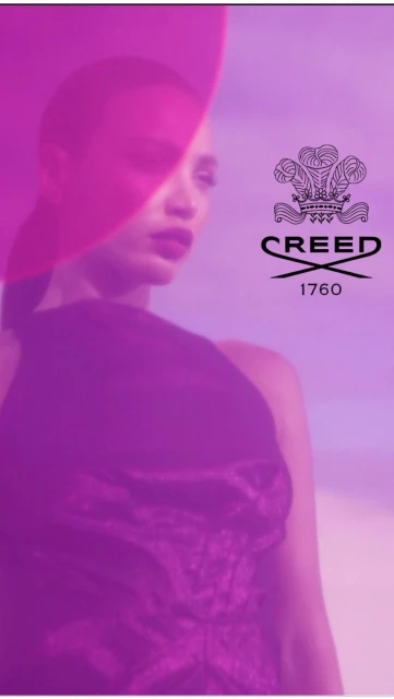 Woman with red lipstick and purple hat poses next to Creed logo in a studio-lit fashion portrait.