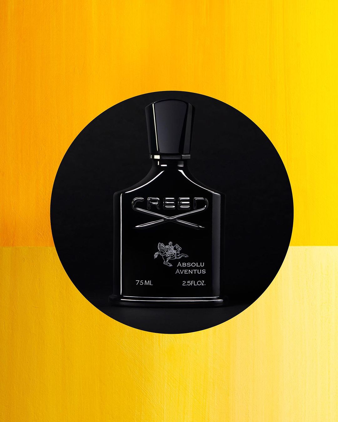 Elegant black Creed Absolu Aventus perfume bottle stands out against a vibrant yellow backdrop and a sleek black circular foreground.