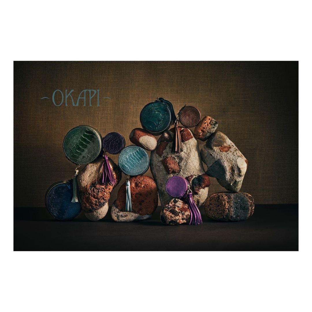 Arrangement of colorful round coin purses with tassels on rustic stones and a canvas backdrop for a textured, organic aesthetic.