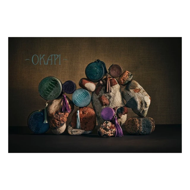 Arrangement of colorful round coin purses with tassels on rustic stones and a canvas backdrop for a textured, organic aesthetic.