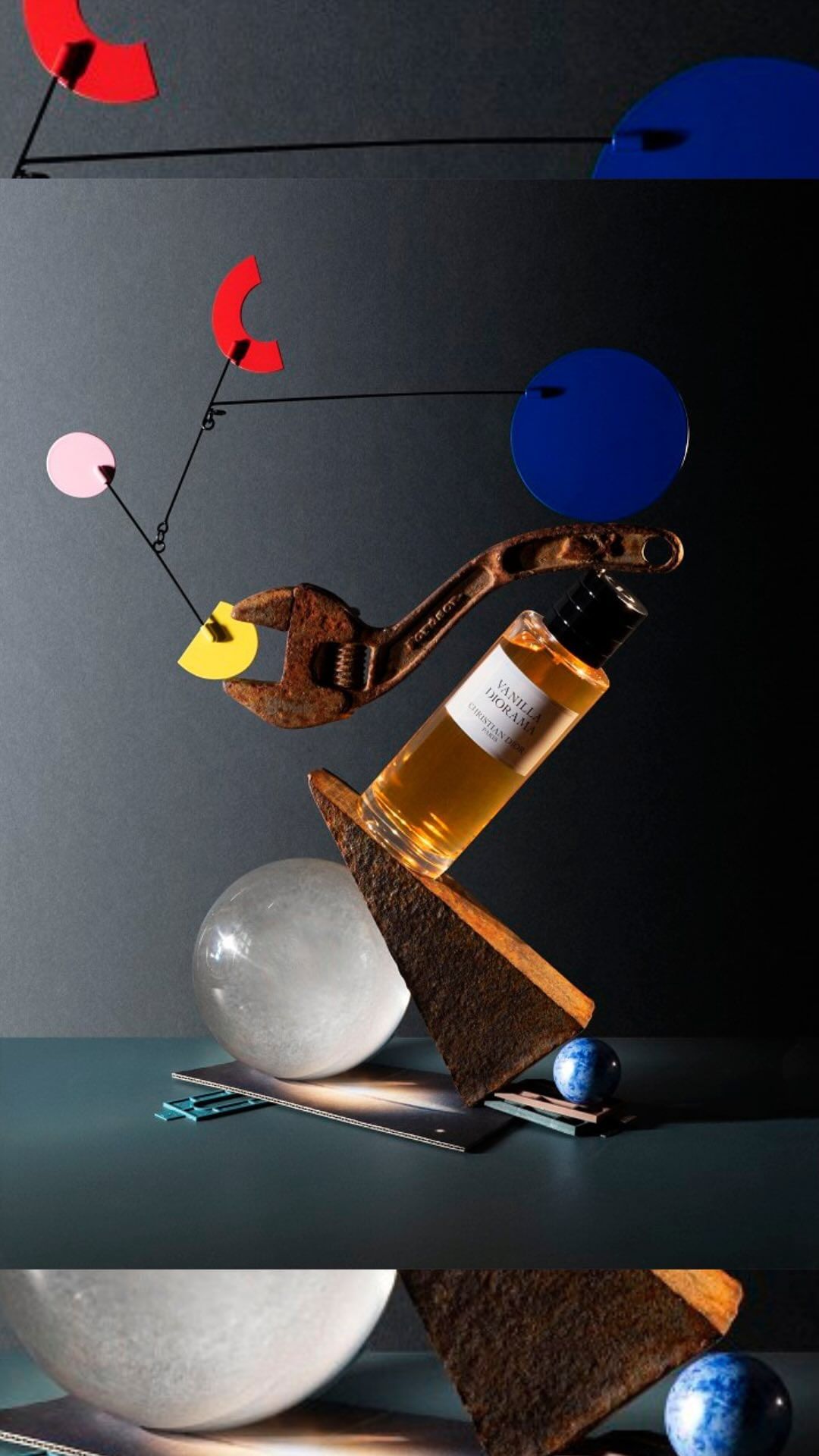 Still life shot featuring a bottle of vanilla dioramas perfume, rusty wrench, colorful geometric shapes, spheres, set against a dark backdrop.