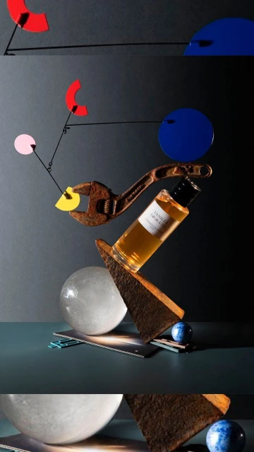 Still life shot featuring a bottle of vanilla dioramas perfume, rusty wrench, colorful geometric shapes, spheres, set against a dark backdrop.
