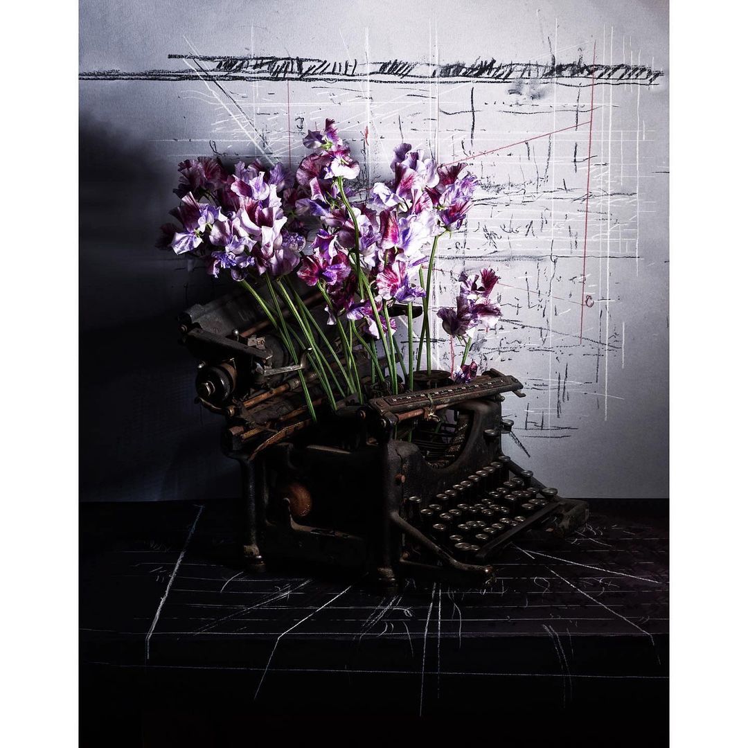 Antique typewriter adorned with vibrant purple flowers against a textured backdrop, creating a captivating contrast of old and new.
