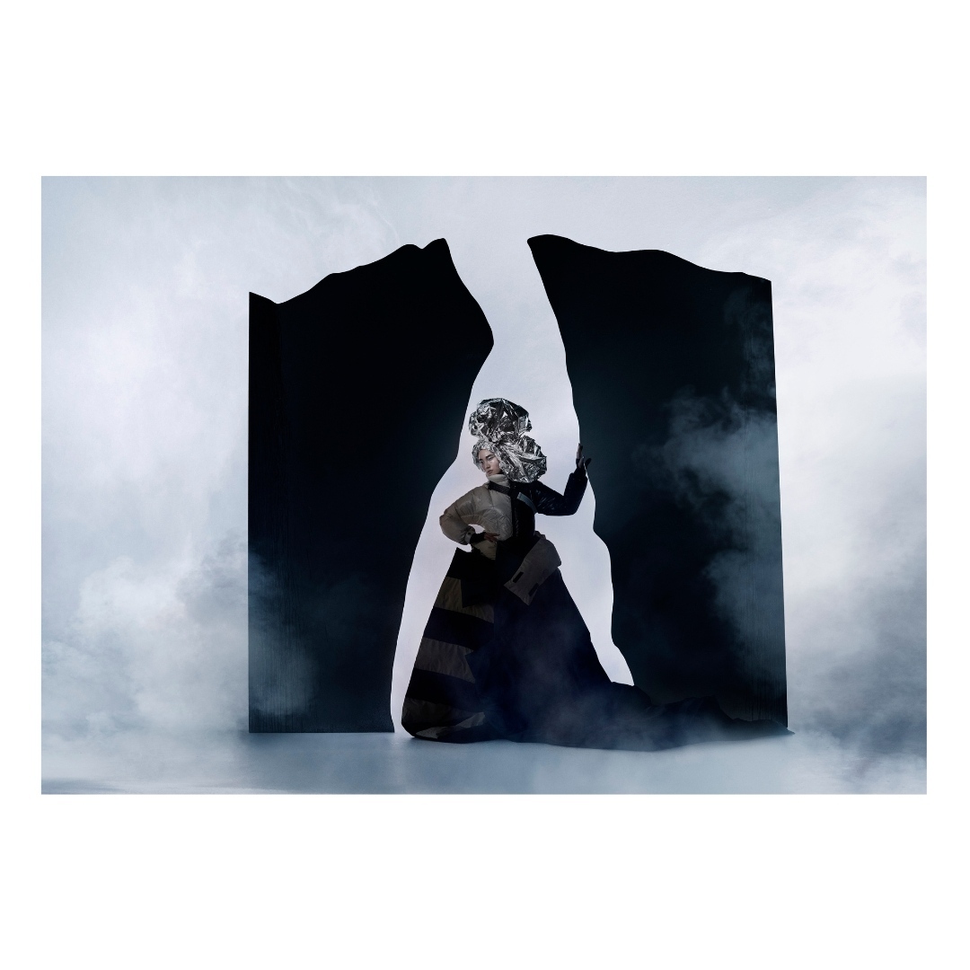 Abstract fashion portrait of a person in a silver headdress and black dress posing in front of a black and white abstract backdrop.
