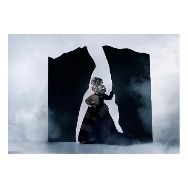 Abstract fashion portrait of a person in a silver headdress and black dress posing in front of a black and white abstract backdrop.
