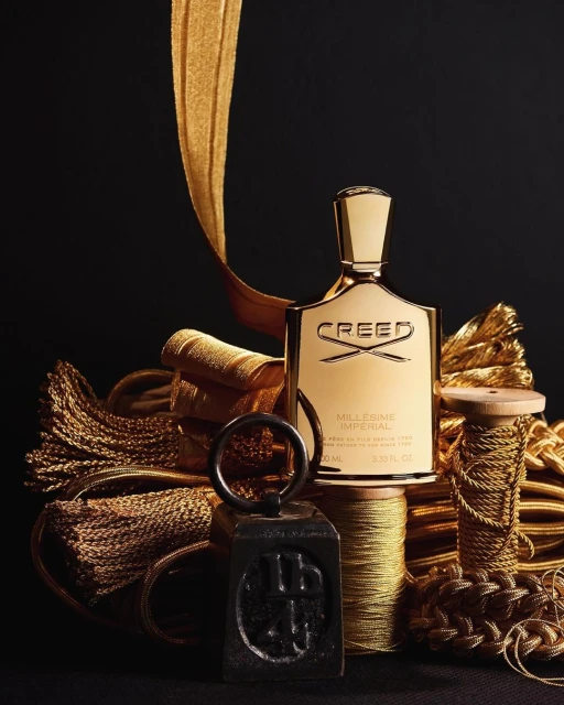 Gold Creed perfume bottle stands out against a black background, surrounded by gold cords, threads, and tassels creating a luxurious feel.