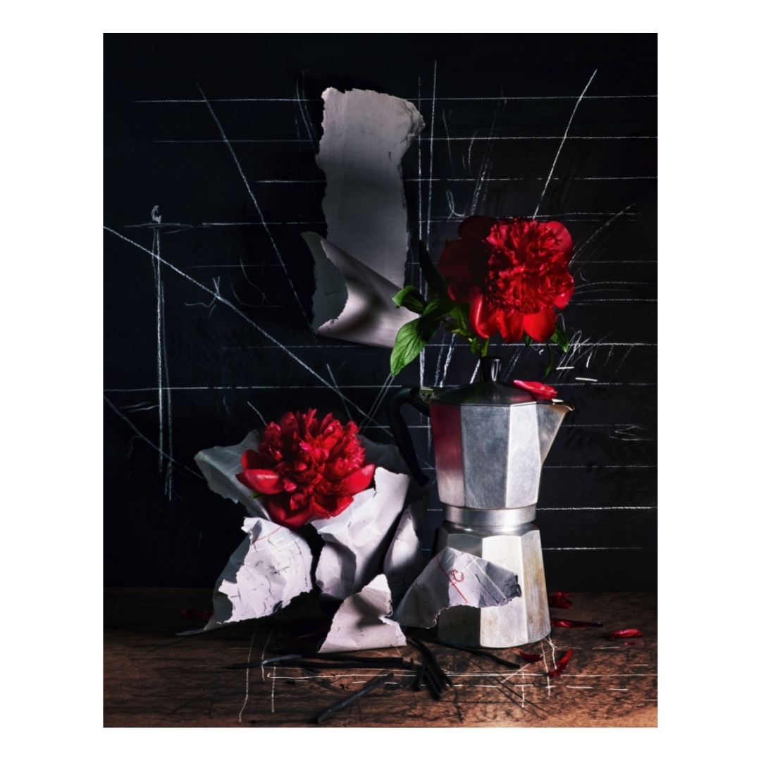 Still life photograph of a moka pot with a red peony flower, set against a dark background with white scribbled lines and paper.