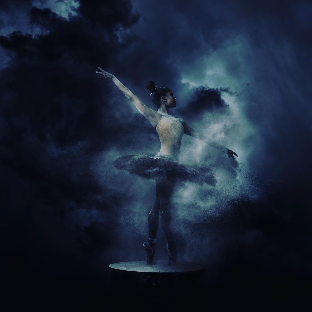 Ballerina strikes a pose in the ethereal blue studio, her tutu suspended in a swirling cloud of powder against a dark backdrop.