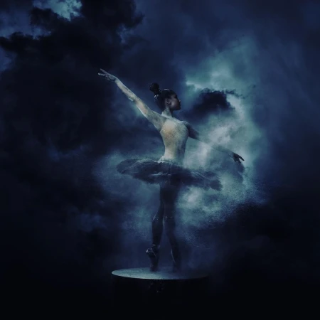 Ballerina strikes a pose in the ethereal blue studio, her tutu suspended in a swirling cloud of powder against a dark backdrop.