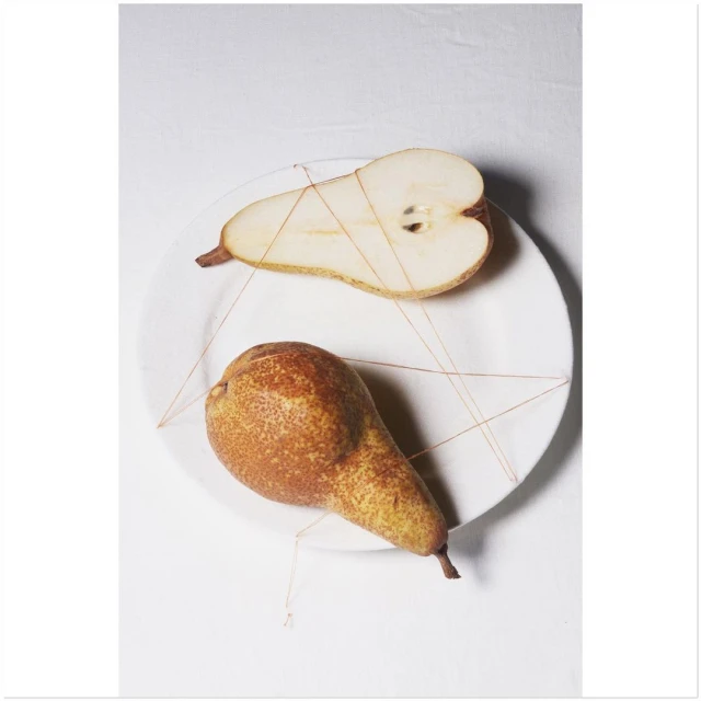 Studio shot of whole and halved pears arranged on a white plate with thin string, lit with soft studio lighting, food photography.