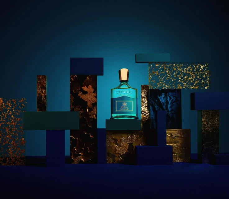 Creed Royal Water fragrance bottle on a blue surface with abstract blocks and textures, creating a luxurious and modern product shot.