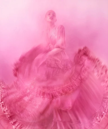 A woman in a flowing pink dress captured with motion blur against a monochrome pink background