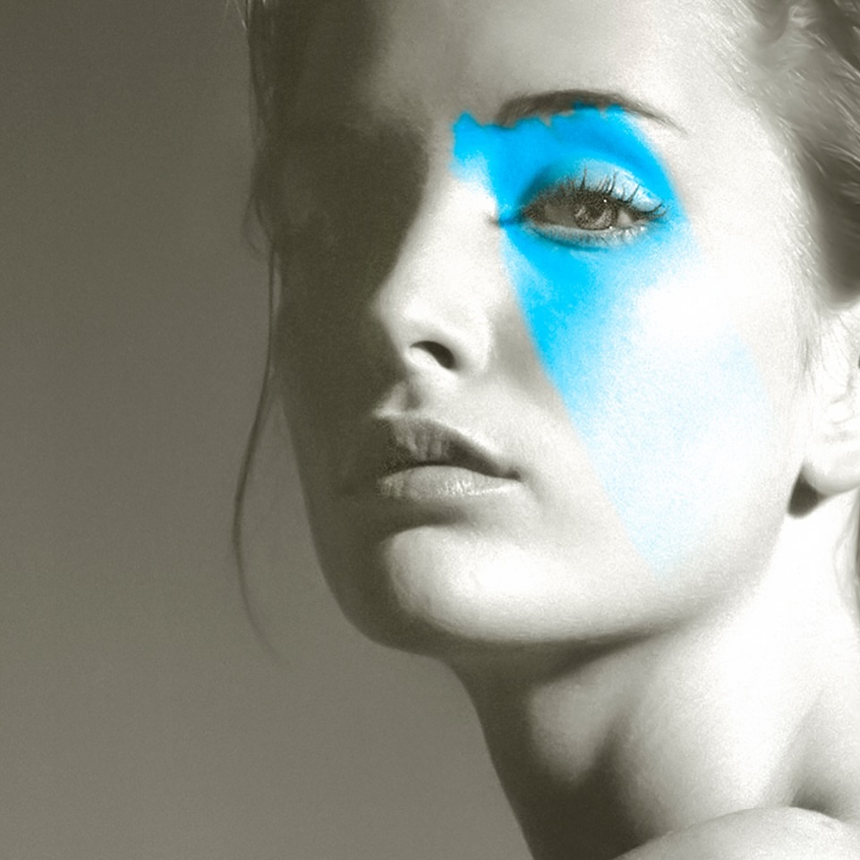 Monochromatic portrait of a fair-skinned woman with bright blue makeup around her eye, creating a striking, artistic beauty image.