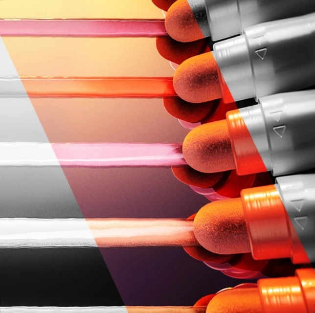Close-up of orange cosmetic applicators with grey handles against a blurred background of gradient colors ranging from pink to orange.