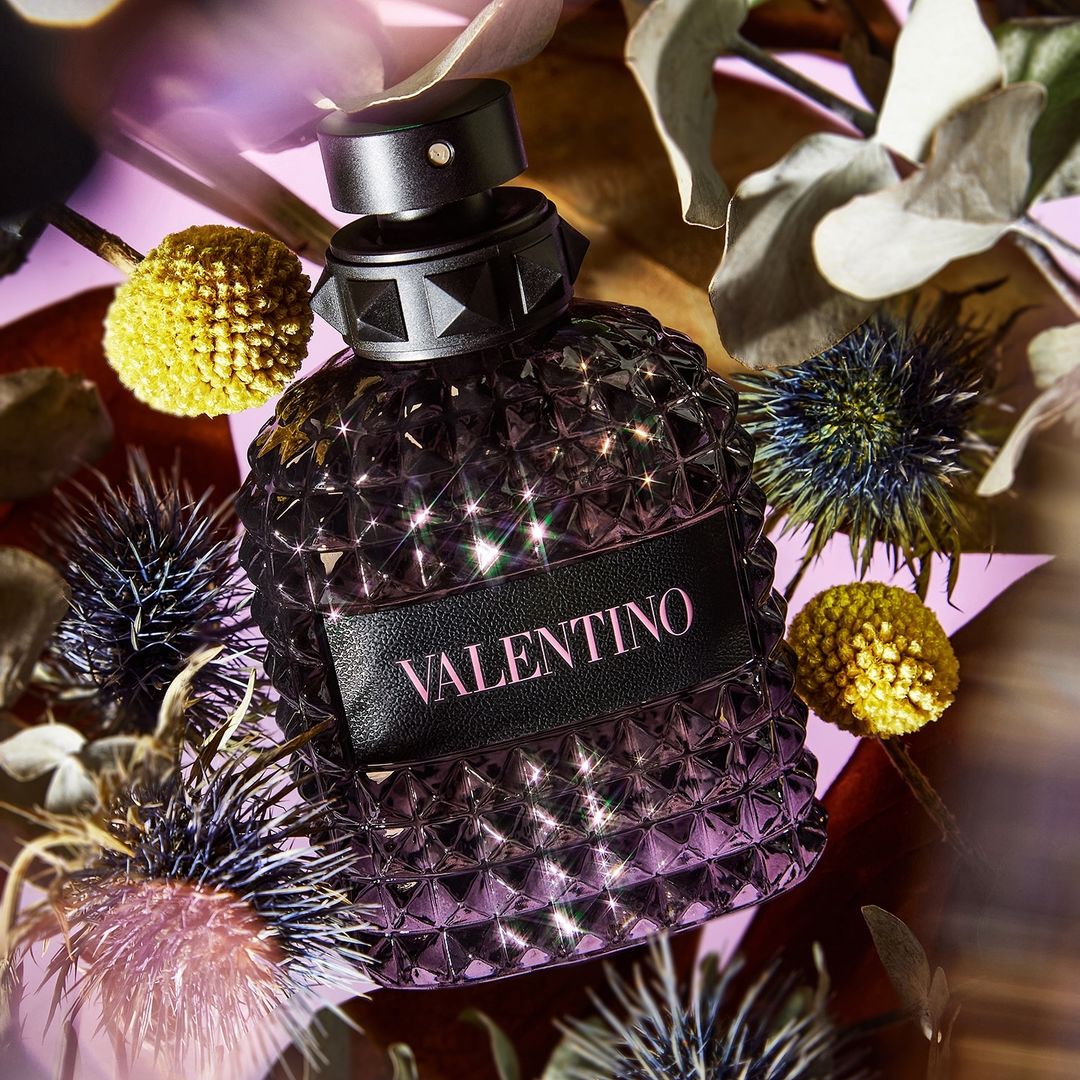 Valentino perfume bottle surrounded by flowers and leaves, product shot on lilac background, beauty and fashion imagery.